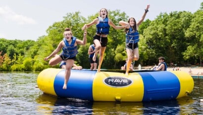 Girls jumping off a water trampoline into the lake.