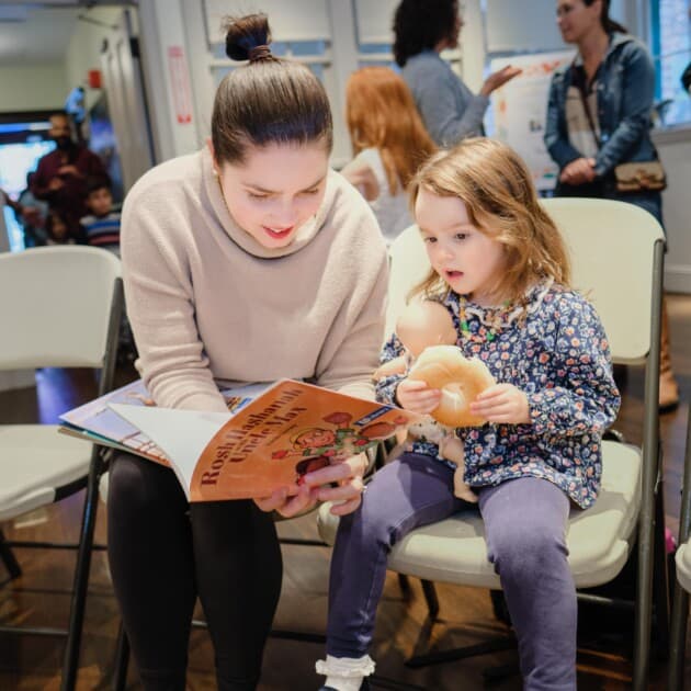 Little girl eats a bagel and listens to a story.