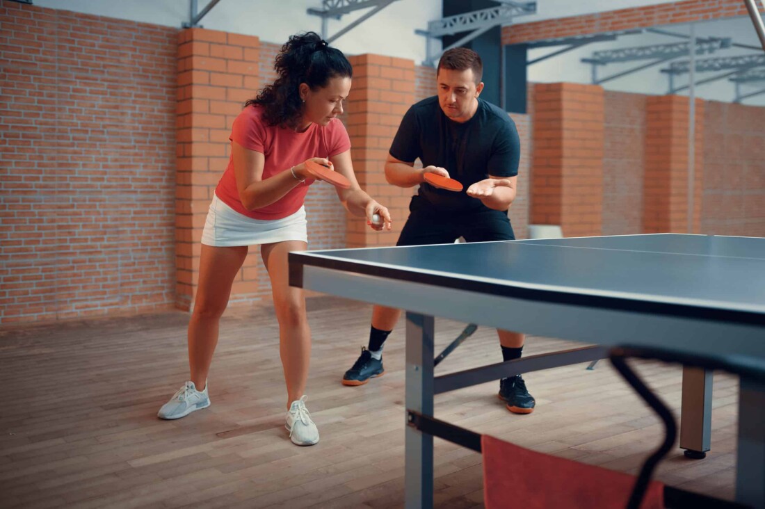 A coach teaching someone how to play table tennis.