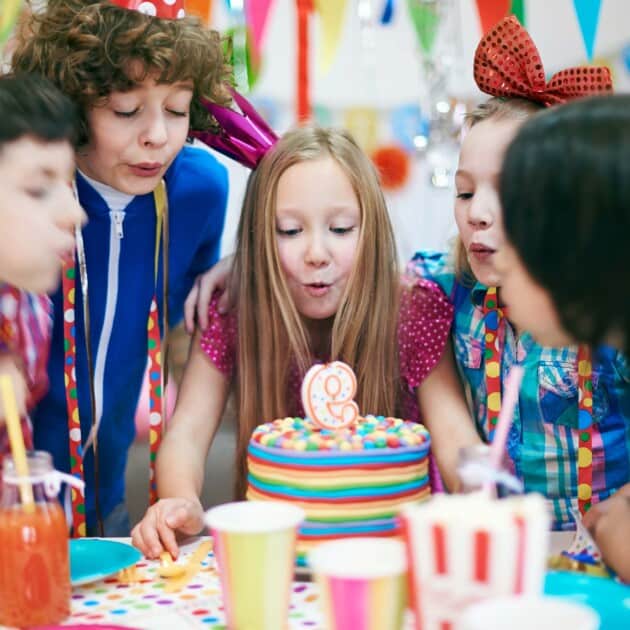 Girl blowing out candles on a cake with friends.