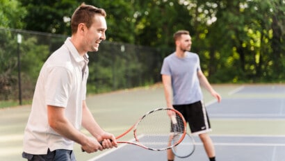 Men playing tennis outdoors in the afternoon.