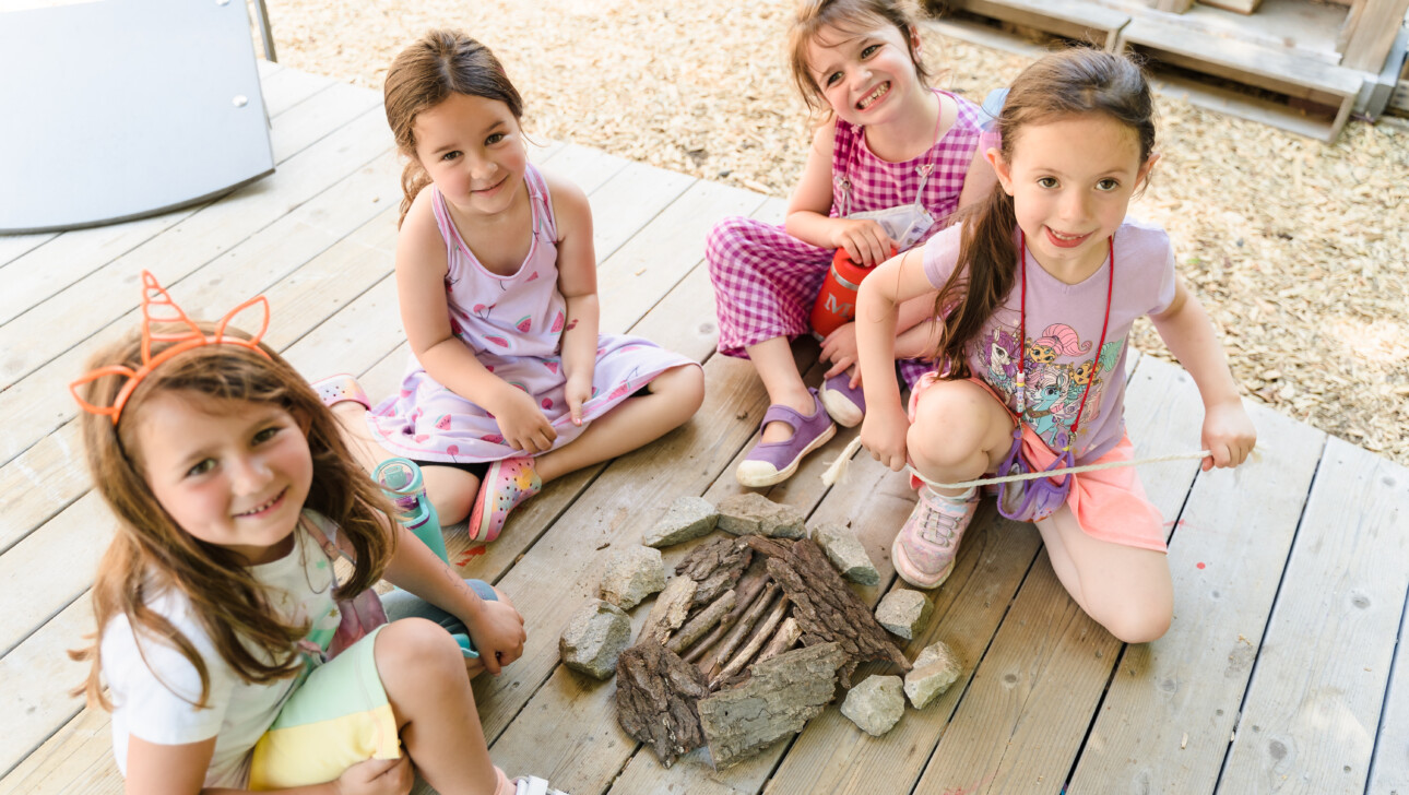 Girls playing with rocks and twigs outside.